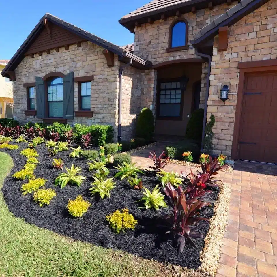 Front beds of yellow and red crotons along a stone-clad home