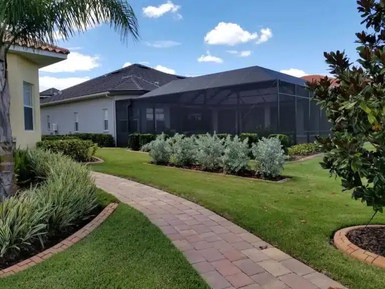 Curved paver walkway through the lawn with silver-leaf shrubs beside a pool enclosure