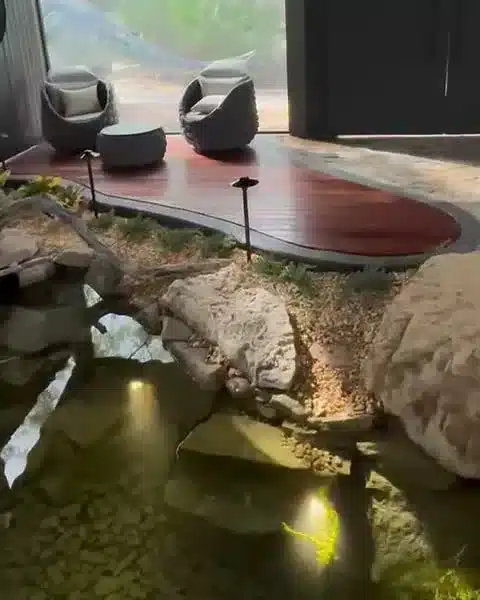 A rock-edged koi pond with small lights glowing under the water inside a screened lanai