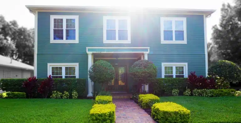 Two-story house with a front lawn, trimmed boxwoods and red cordylines along a brick path