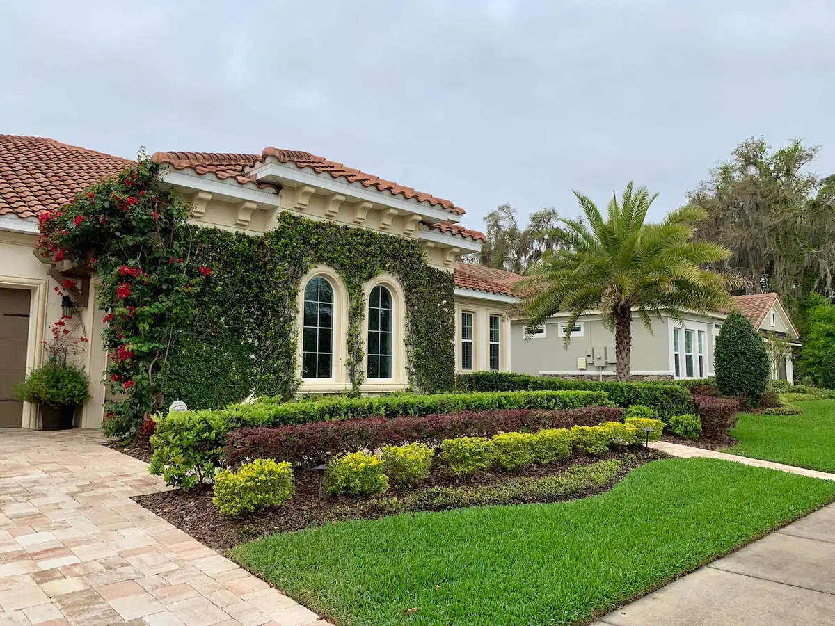 Tan pavers running from the drive to the front door of a tile-roofed house, edged by clipped hedges and lawn