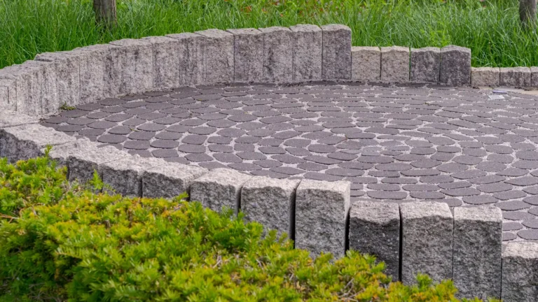 A round patio of gray pavers laid in arcs, ringed by a low wall of upright stone blocks with shrubs in front