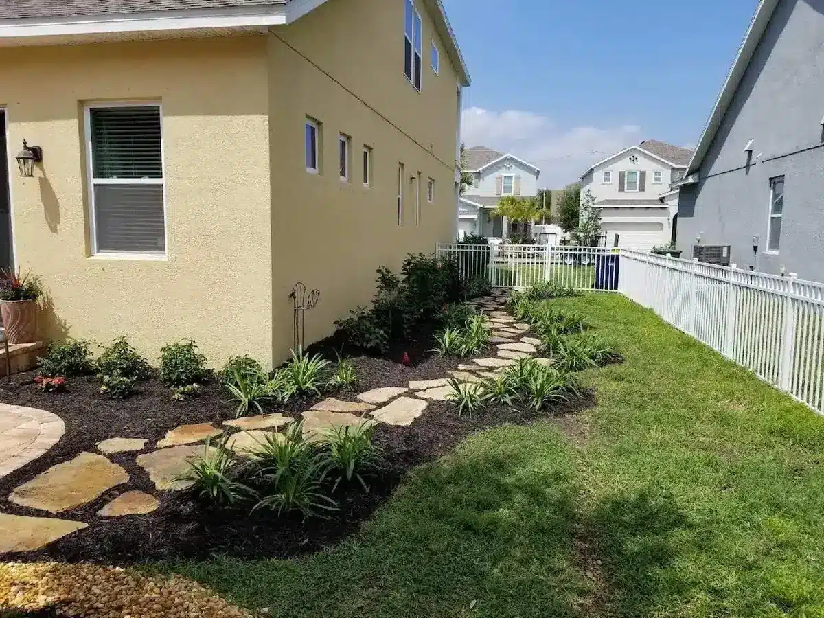 A narrow side yard between two houses with a lawn strip, a fence and a mulched bed with flagstone stepping stones